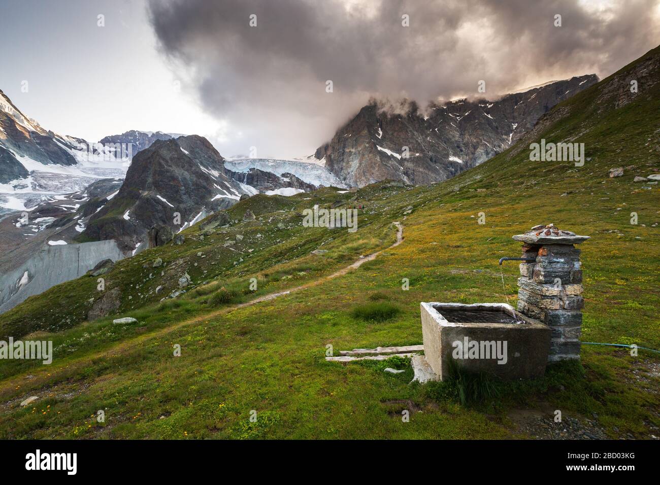 Paysage alpin avec fontaine en pierre. Vue sur le glacier Stockji. Vallée de Zmutt. Zermatt, Valais, Alpes suisses. Suisse. Banque D'Images