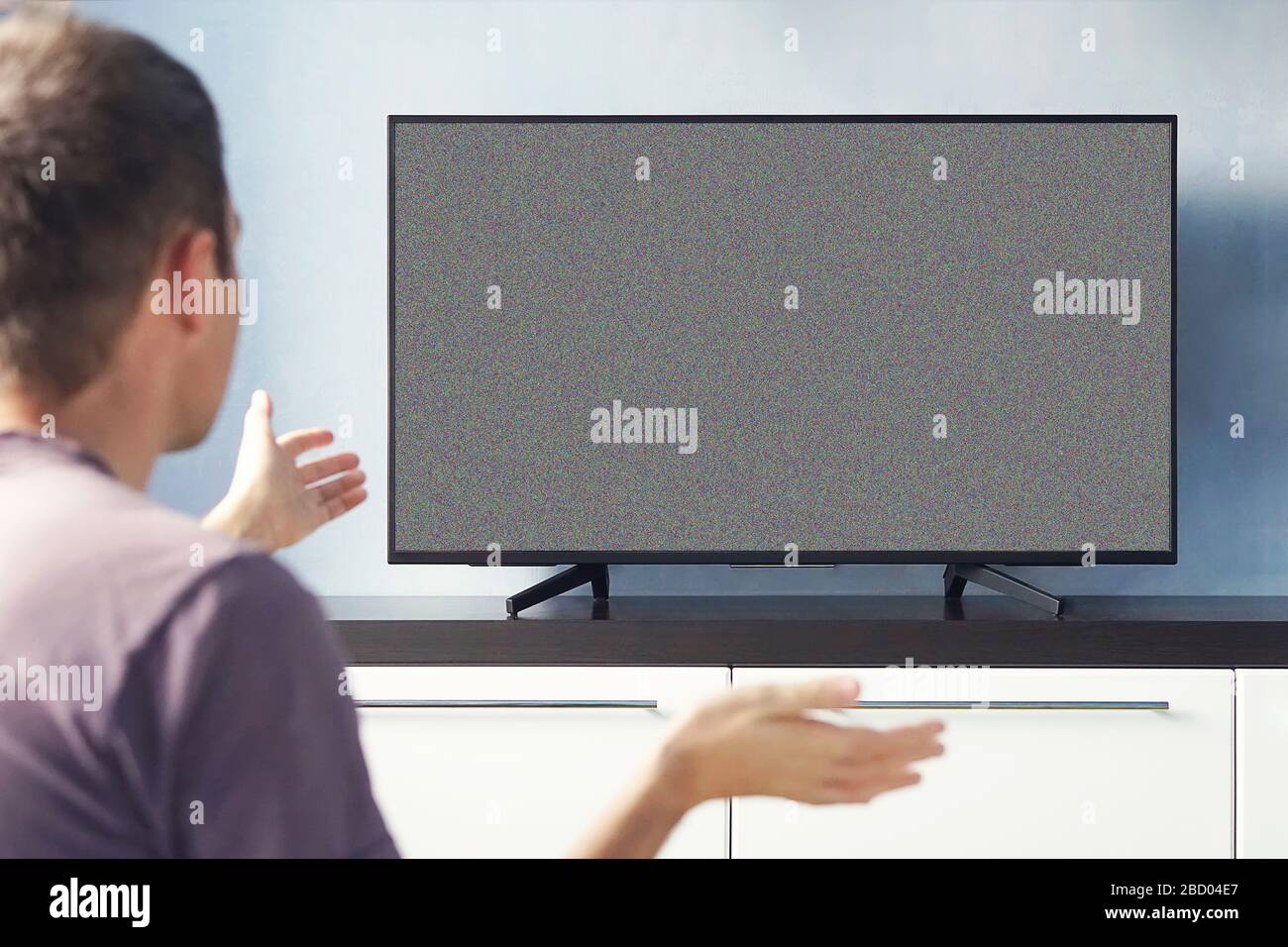 Frustré homme assis sur un canapé devant la télévision sans aucun signal. Jeune homme émotionnellement regardant la télévision et agitant ses mains dans le mécontentement. Banque D'Images