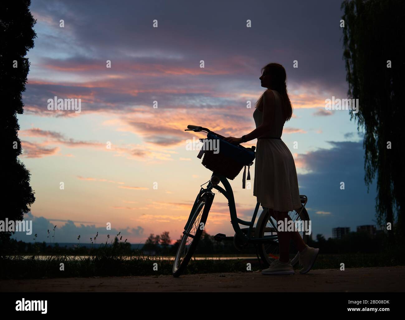 Femme dans une robe légère avec un vélo rétro sous le ciel au coucher du soleil. Profitez d'une vue magnifique sur le ciel du soir avec des nuages colorés en été. Le concept de liberté et de détente Banque D'Images