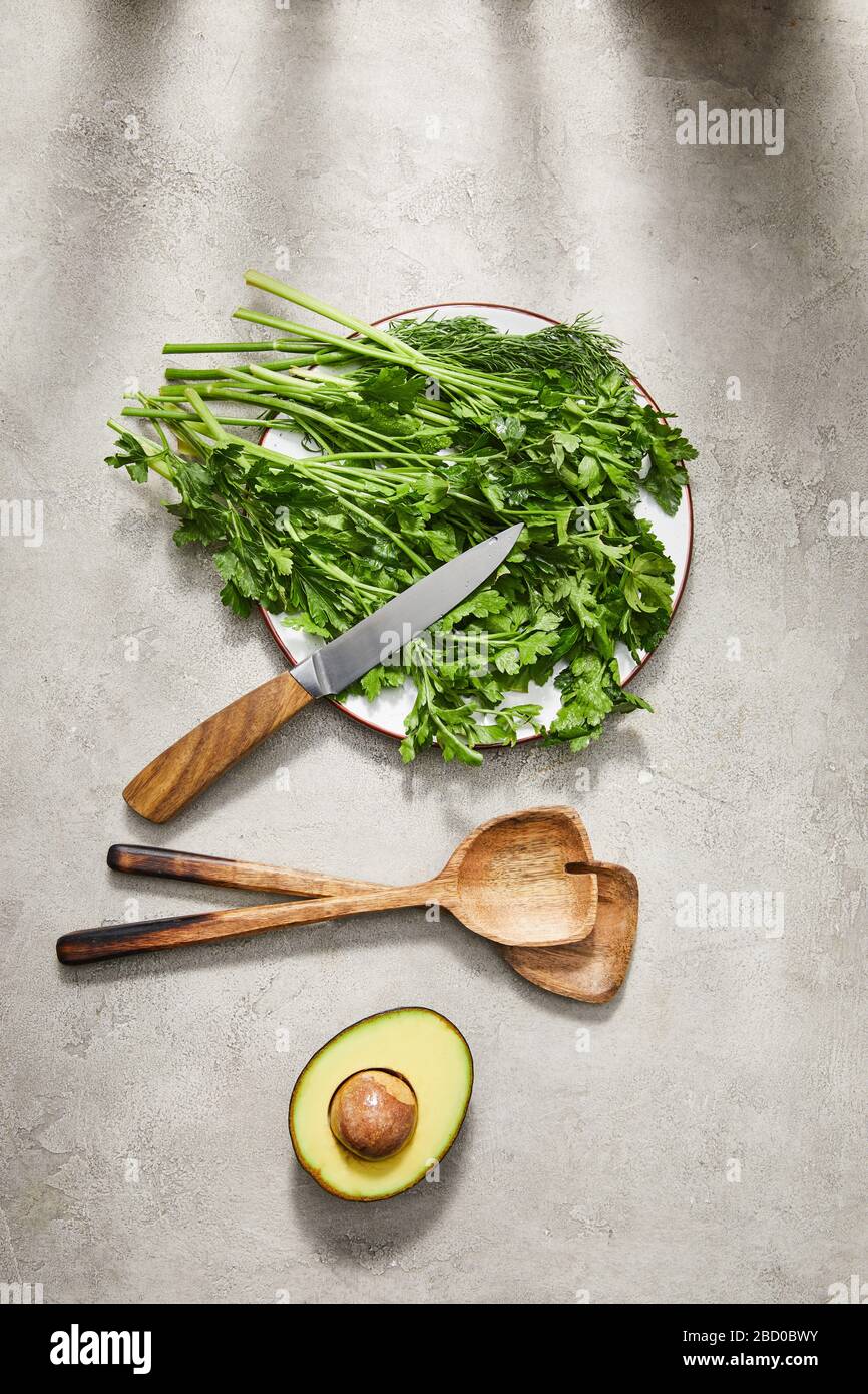 Vue de dessus de la verdure sur la plaque, le couteau, les spatules et les moitiés d'avocat sur fond gris Banque D'Images