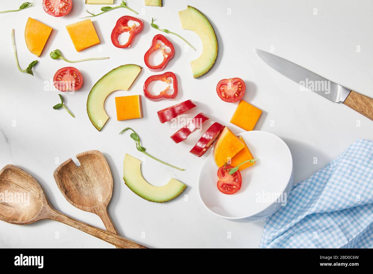 Vue de dessus du bol avec microgreens, légumes coupés et tranches d'avocat près du couteau, spatules et tissu sur blanc Banque D'Images