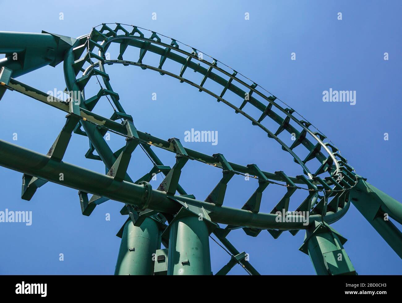 Montagnes russes incurvées dans un parc à thème ou d'attractions, pistes métalliques vertes vides et fond bleu ciel. Banque D'Images