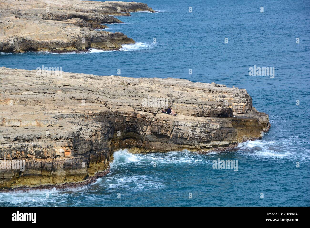 Falaises spectaculaires dans la mer Adriatique avec des vagues qui frappent le rocher de Polignano a Mare; un touriste appréciant le moment; la ville est important mostl Banque D'Images