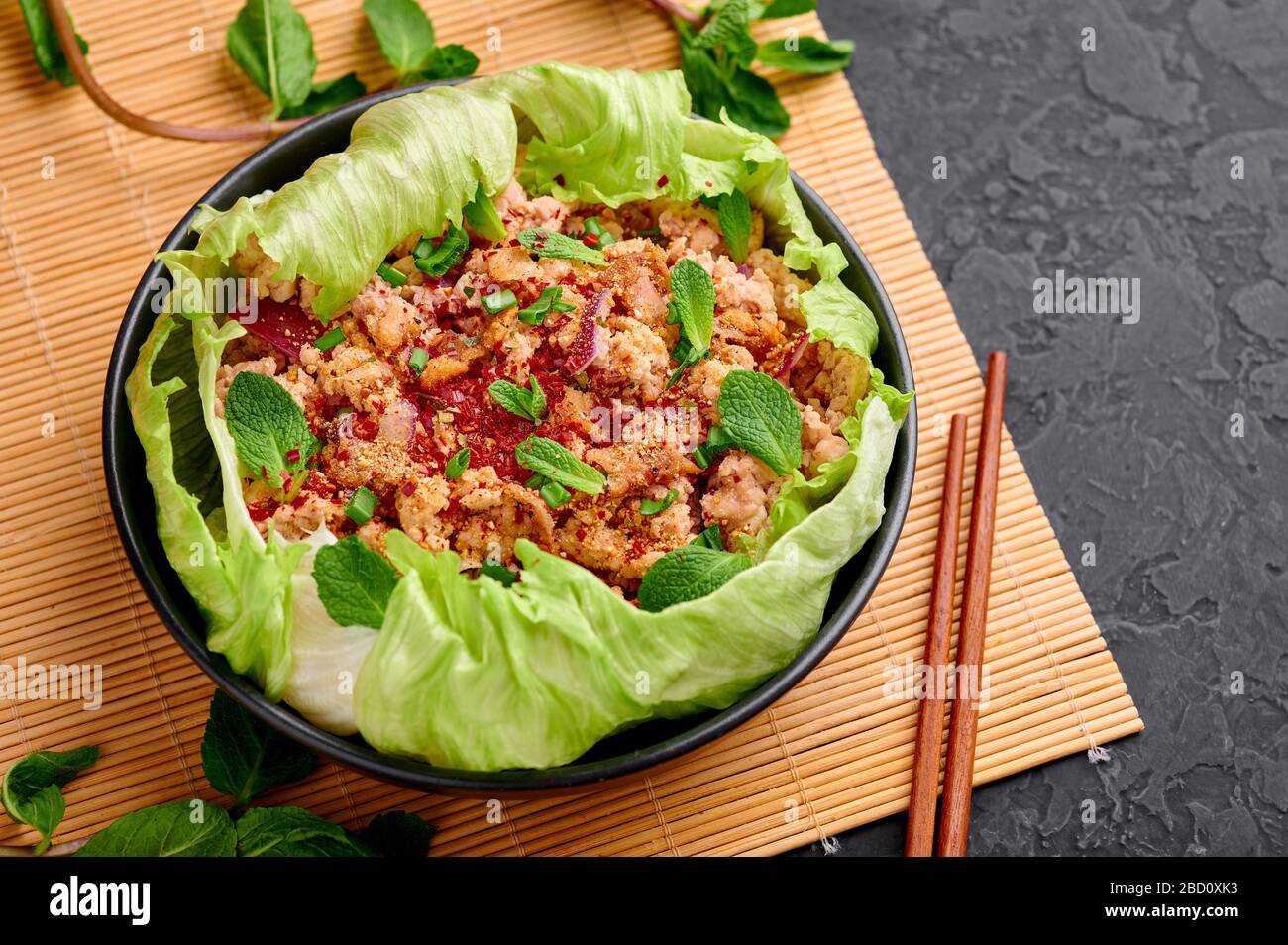 Laab Gai - salade de poulet hachée thaï dans un bol noir sur fond d'ardoise  sombre. Larb est un plat de cuisine thaïlandaise avec de la viande hachée,  de la sauce au