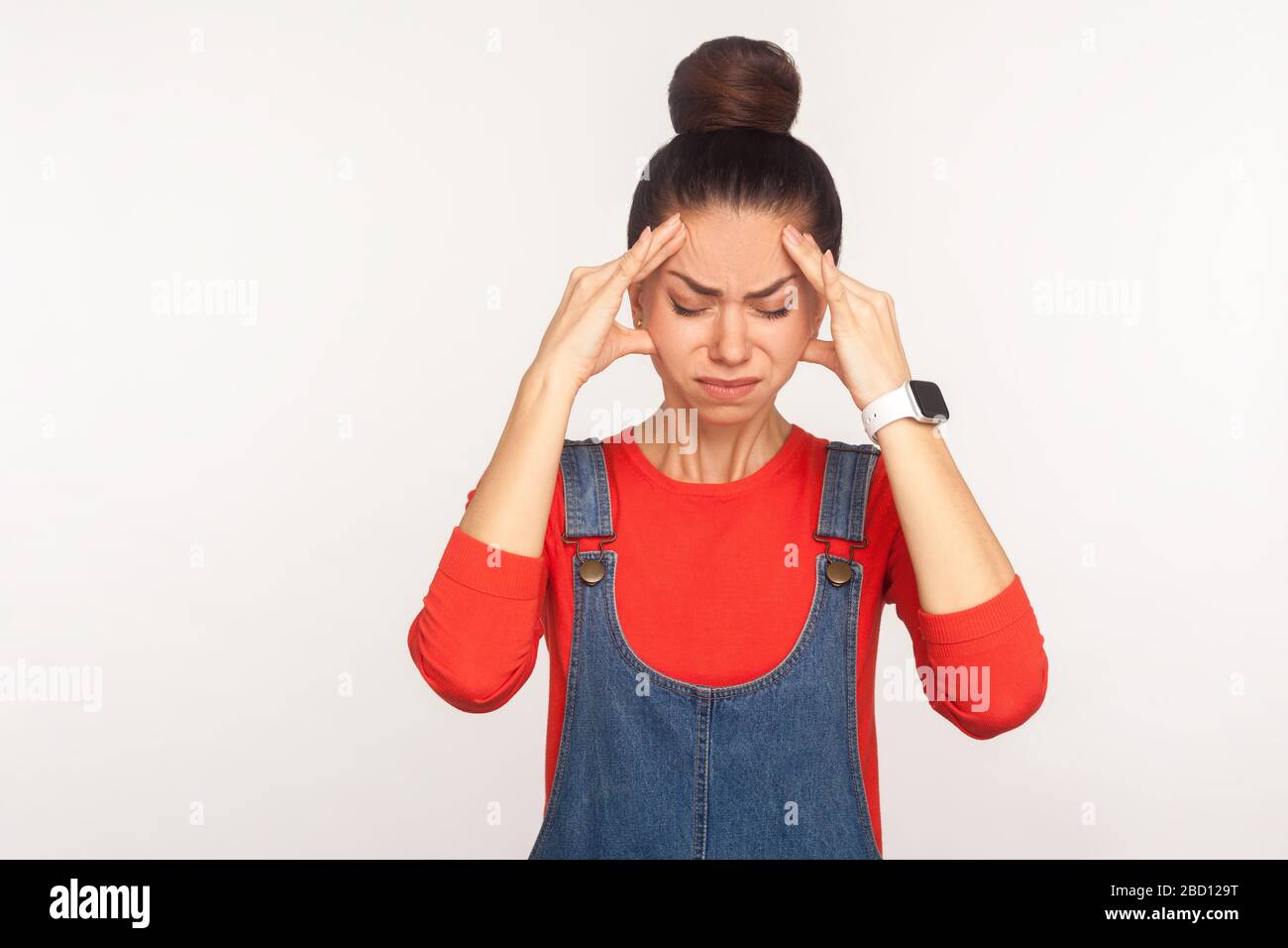 Maux de tête. Portrait d'une fille déprimée fatiguée avec un pain de cheveux dans des salopettes en denim se sentant malsain, souffrant de migraine et de tension, méningite, grippe sy Banque D'Images