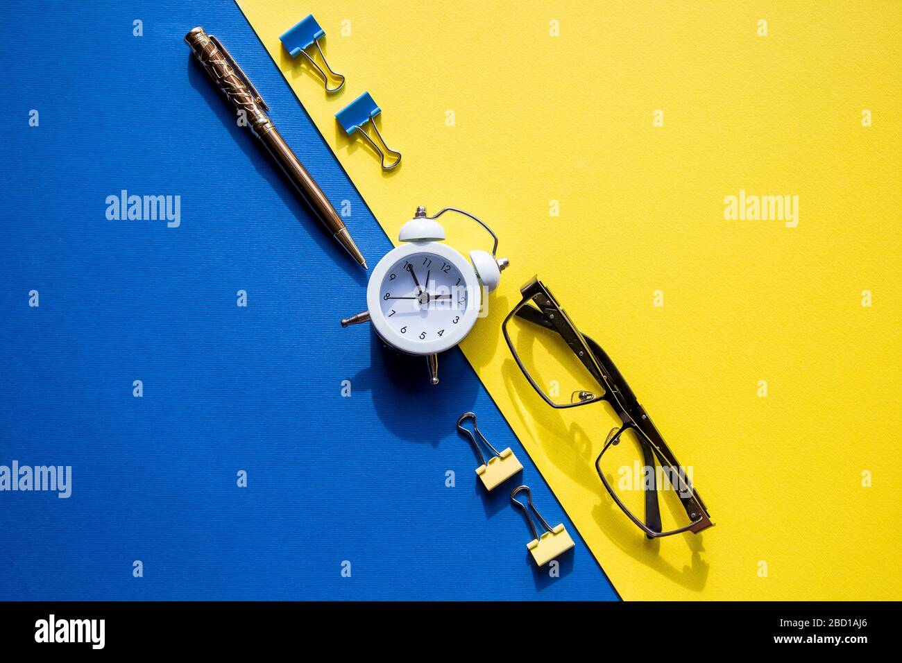 stylo doré, lunettes élégantes, clips pour papier et réveil sur fond coloré Banque D'Images