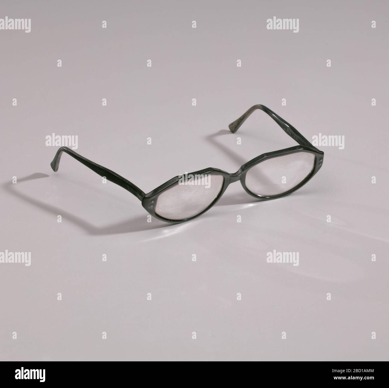 Lunettes de la boutique Maes Millinery. Une paire de lunettes bifocales  avec cadres en plastique noir. Les lentilles sont légèrement ovulaires avec  un bord inférieur lisse et un bord supérieur à deux