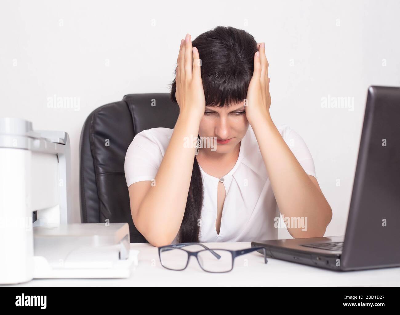 Une fille est assise dans un bureau d'affaires et tient sur sa tête. Le concept de crise et la baisse des bénéfices pendant la pandémie de coronavirus. COVID-19 et Banque D'Images