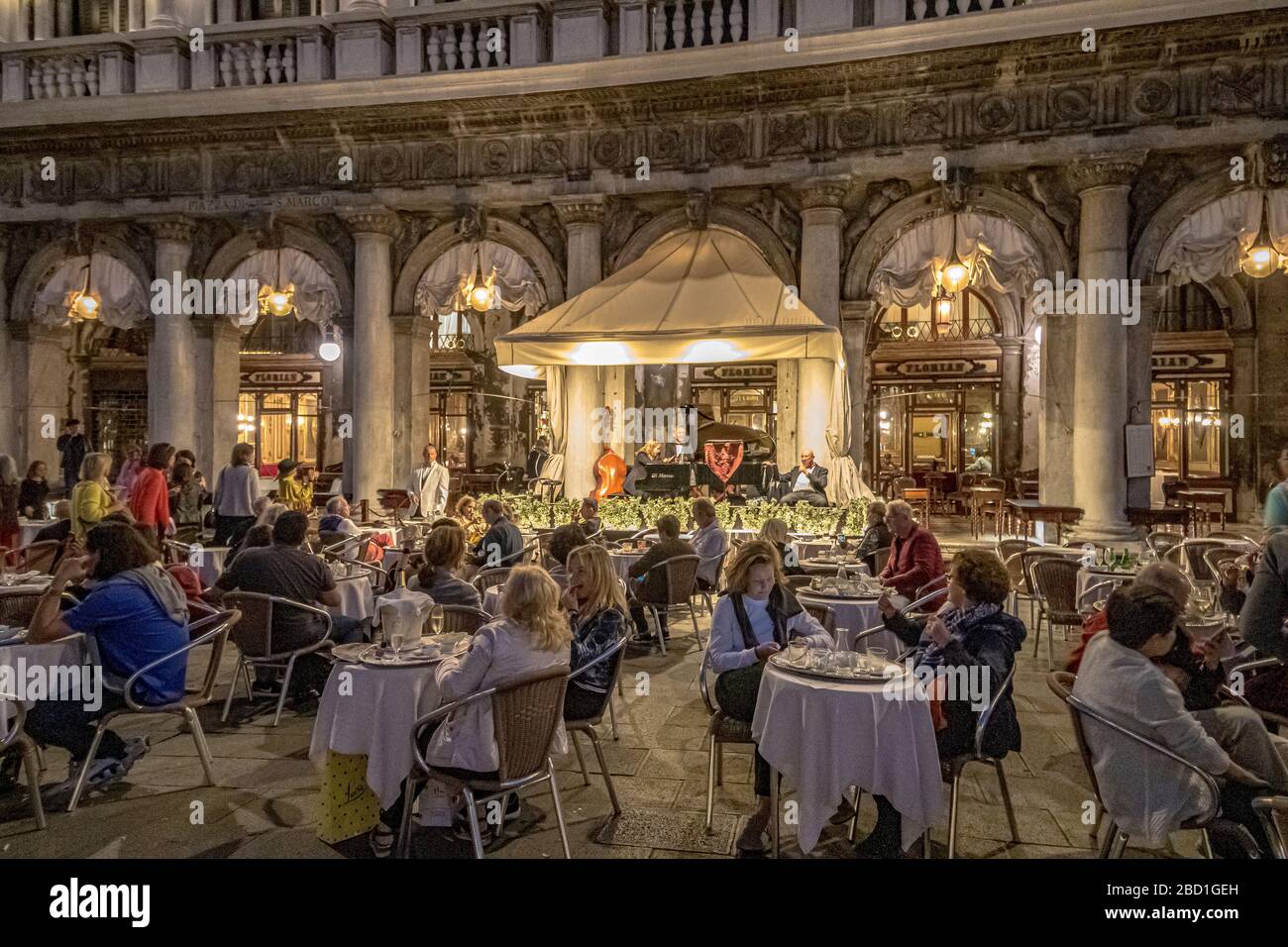 Les gens assis à l'extérieur de Caffè Florian un café célèbre au coeur de la place Saint-Marc comme le groupe résident joue en début de soirée, Venise Italie Banque D'Images