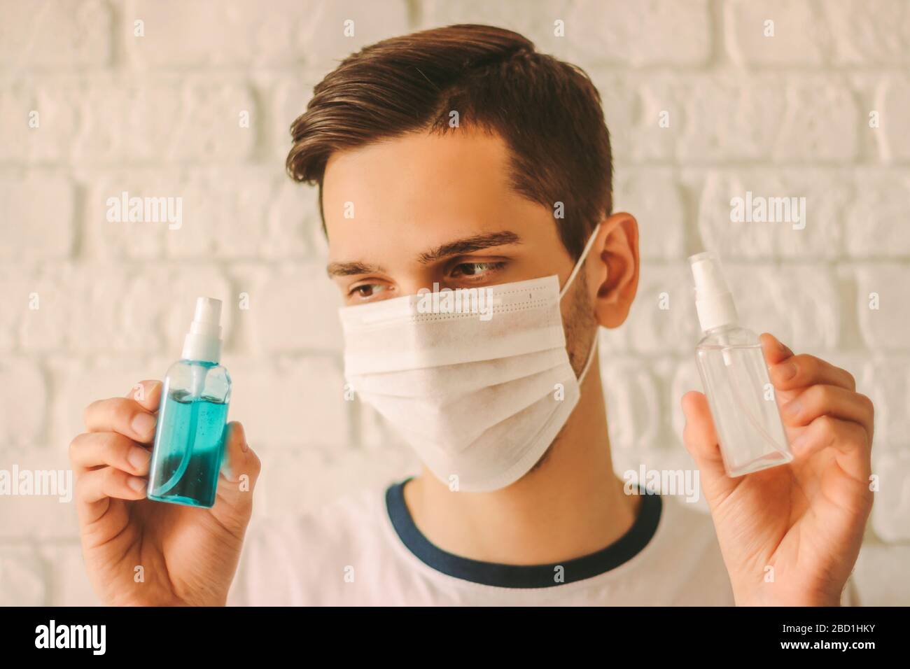 Jeune homme dans le masque médical sur le visage montrant des bouteilles de gel antibactérien. Médecin confiant dans le masque protecteur qui maintient les désinfectants dans les mains. hy personnel Banque D'Images