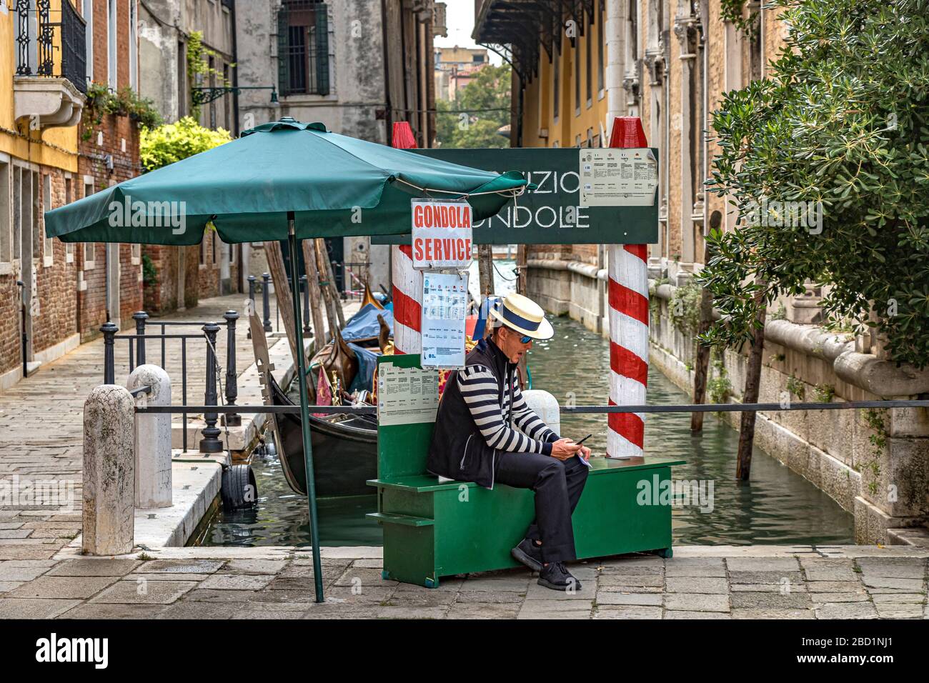 Un gondolier assis en regardant son téléphone mobile tout en attendant que les touristes prennent une télécabine à Campo Santo Stefano, Venise, Italie Banque D'Images