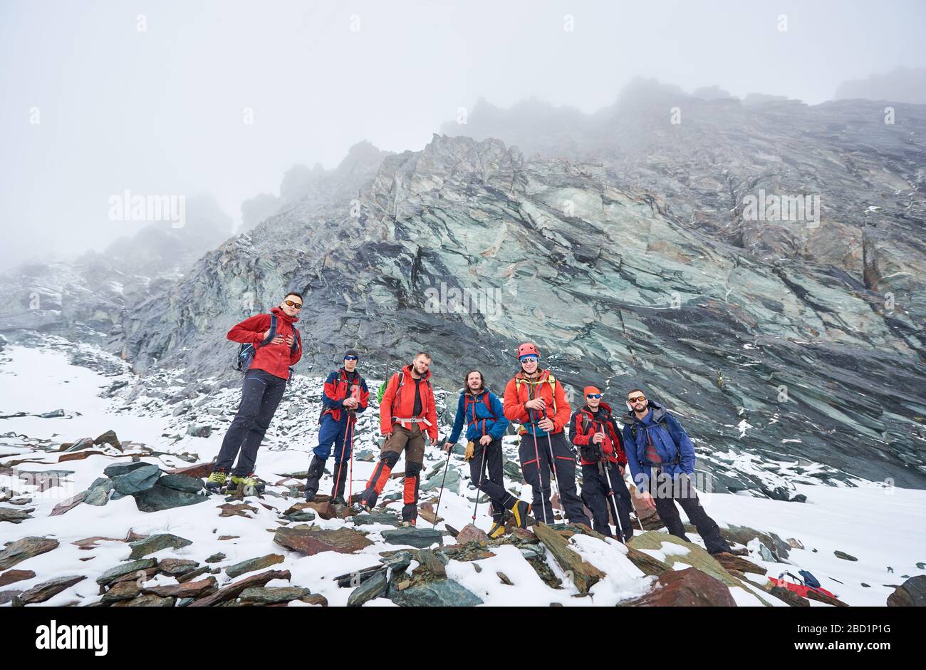 Des alpinistes masculins se tenant sur les rochers et les pierres tout en prenant la rupture de la randonnée dans les montagnes d'hiver. Équipe de randonneurs avec bâtons de randonnée regardant l'appareil photo. Concept de voyage, de randonnée et d'alpinisme. Banque D'Images