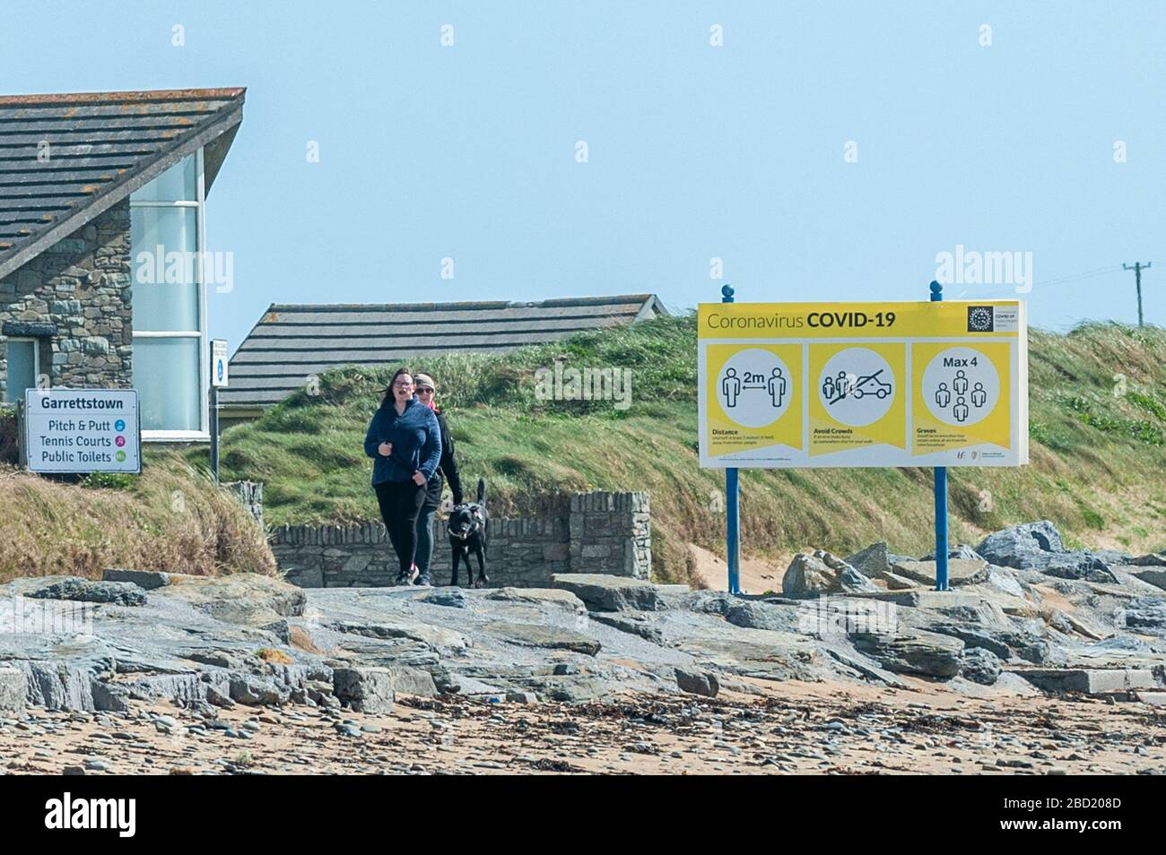 Garrettstown, West Cork, Irlande. 6 avril 2020. Deux femmes marchent leur chien devant un panneau d'information Covid-19 à Garrettstown Beach aujourd'hui. Crédit : Andy Gibson/Alay Live News Banque D'Images