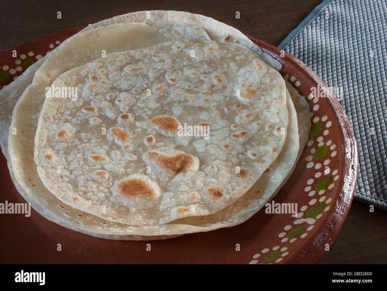 Tortillas de farine sur une plaque mexicaine d'argile ou une plaque de boue avec une serviette bleue sur le côté avec lumière de jante Banque D'Images