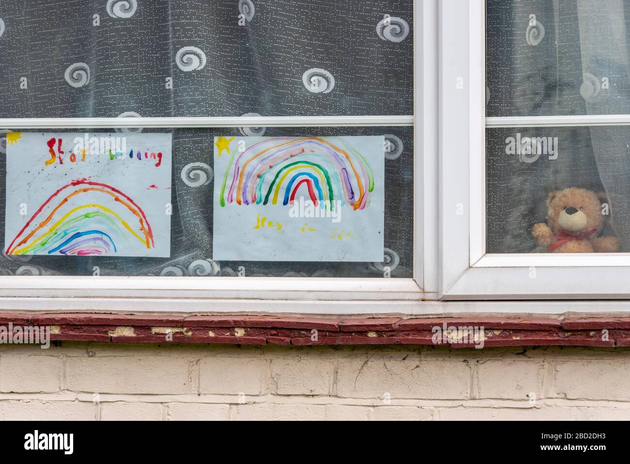 L'art arc-en-ciel et l'ours en peluche de l'enfant dans la fenêtre de la maison pendant la période de verrouillage pandémique du COVID-19 Coronavirus. Chasse aux ours en peluche, sentier arc-en-ciel Banque D'Images