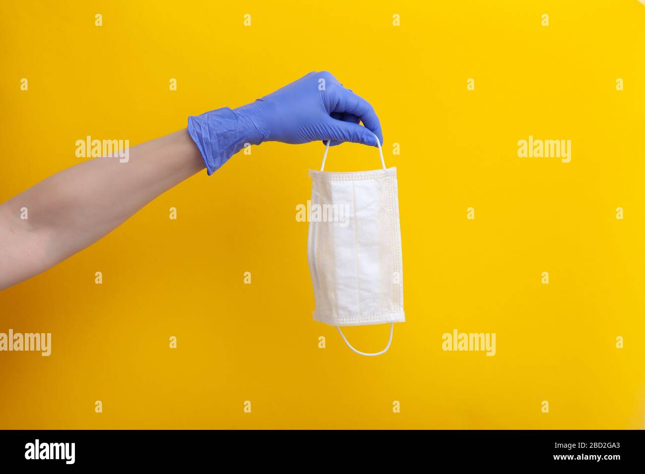 Masque médical jetable blanc pour prévenir l'infection du coronavirus respiratoire dans la main femelle dans le gant en latex de caoutchouc sur fond jaune, horizontal, cop Banque D'Images