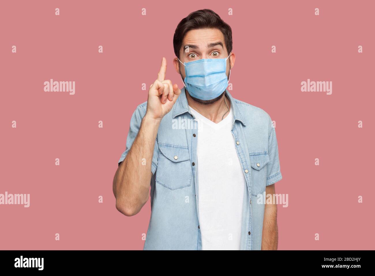 J'en ai une idée. Portrait de jeune homme surpris avec masque médical chirurgical en chemise bleue debout avec le visage étonné, regardant l'appareil photo avec le signe de l'idée. Banque D'Images