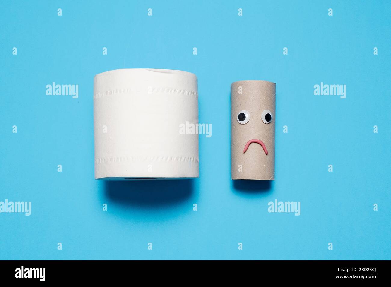Rouleau plein de papier toilette à côté d'un rouleau vide triste et frognant avec des yeux et la bouche sur un fond bleu avec espace de copie et de la place pour le texte Banque D'Images