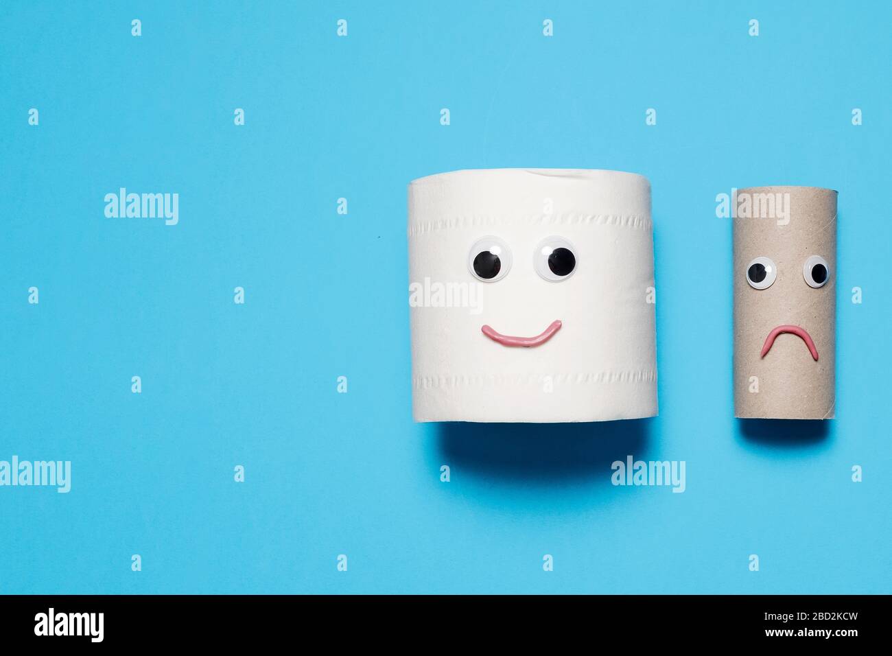 Joyeux sourire plein rouleau de papier toilette à côté de triste rouleau vide avec des yeux et de la bouche googly sur un fond bleu avec espace de copie et de la place pour le texte Banque D'Images