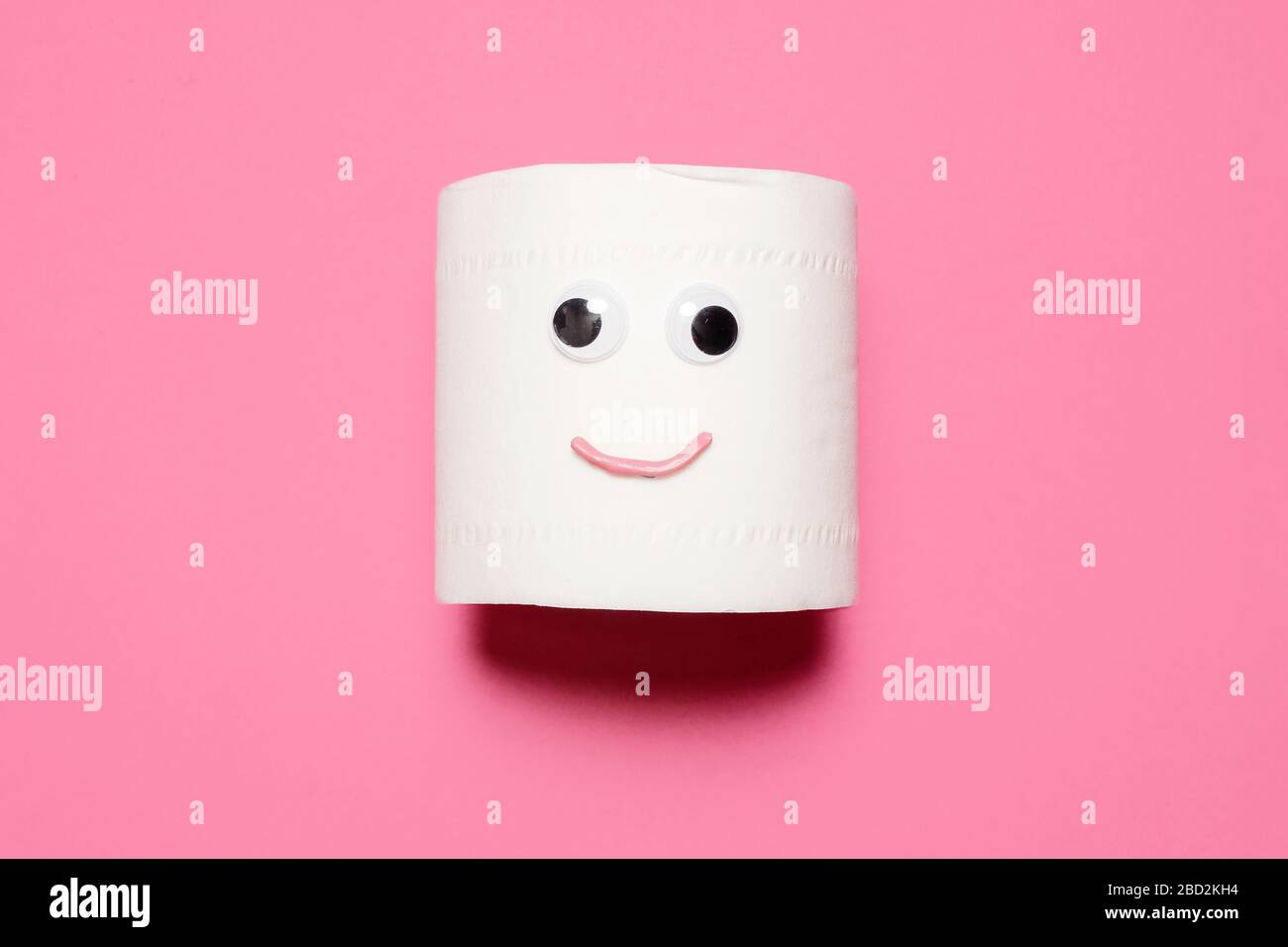 Joyeux sourire plein rouleau de papier toilette avec des yeux et la bouche googly sur un fond rose avec espace de copie et de la place pour le texte Banque D'Images