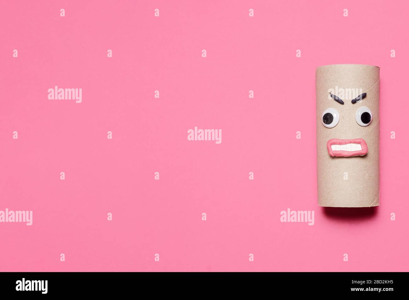 Rouleau vide en colère de papier toilette avec des yeux googly, la bouche et les sourcils sur un fond rose avec espace de copie et de la place pour le texte Banque D'Images