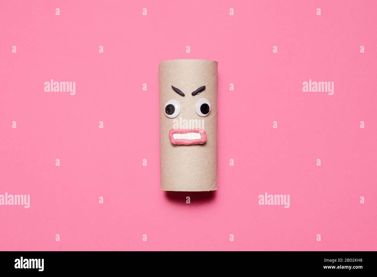 Rouleau vide en colère de papier toilette avec des yeux googly, la bouche et les sourcils sur un fond rose avec espace de copie et de la place pour le texte Banque D'Images