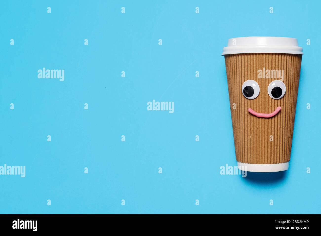 Tasse à café en papier brun et en plastique avec yeux google et visage heureux sur un fond bleu avec espace de copie et de la place pour le texte. Banque D'Images