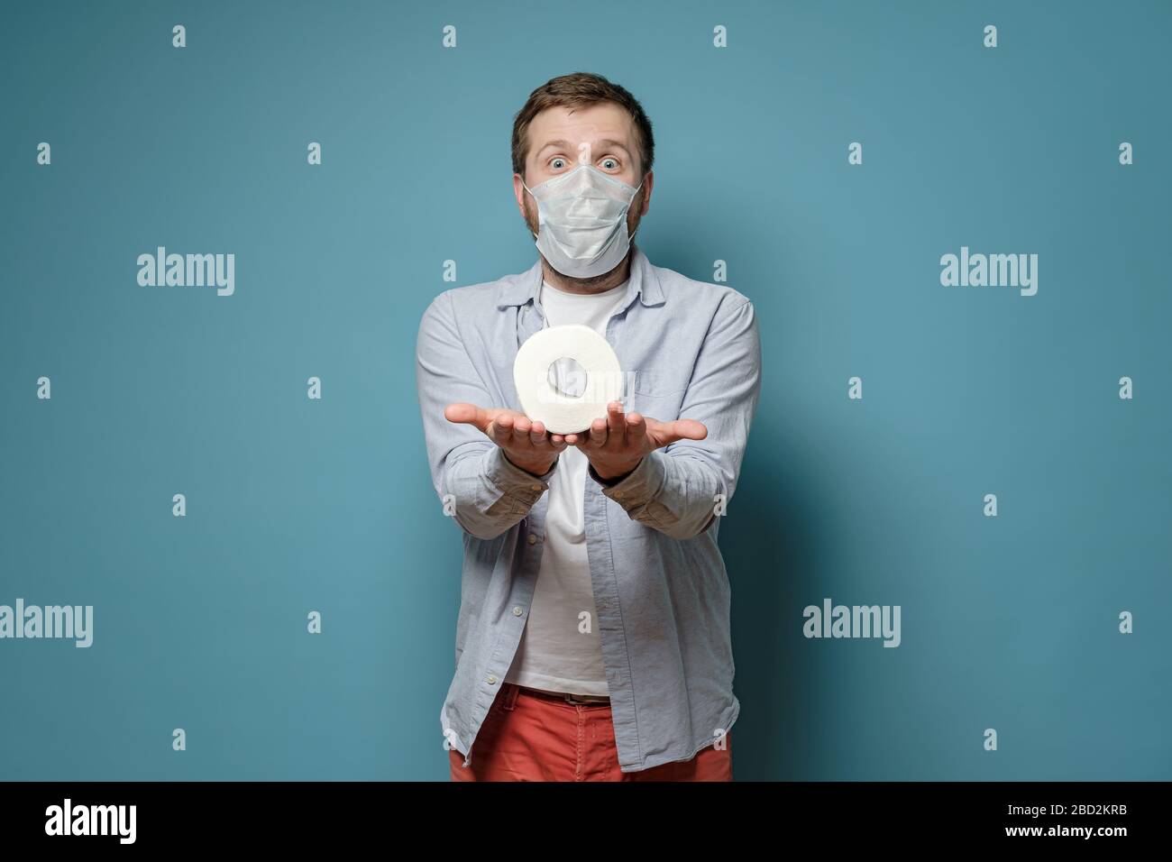 Homme dans un masque médical tenant du papier toilette sur les paumes et regardant joyeusement. Concept de pénurie de biens pendant une épidémie de virus. Banque D'Images