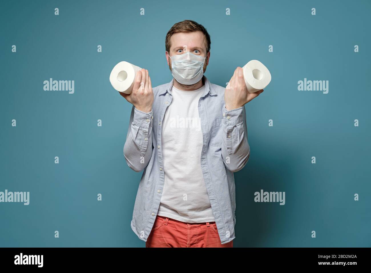 L'homme joyeux dans un masque médical tient dans des mains papier toilette, qu'il a réussi à acheter pendant une épidémie de virus et une pénurie de marchandises. Banque D'Images