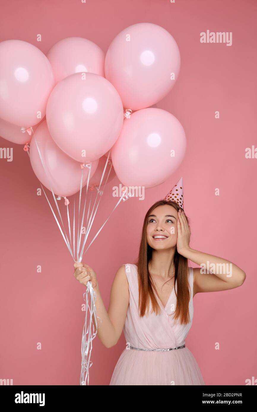 Belle surprise heureuse femme en robe et chapeau d'anniversaire célébrant  avec des ballons d'air rose pastel isolés sur fond rose. Jolie jeune fille  heureuse lors d'une fête d'anniversaire Photo Stock - Alamy
