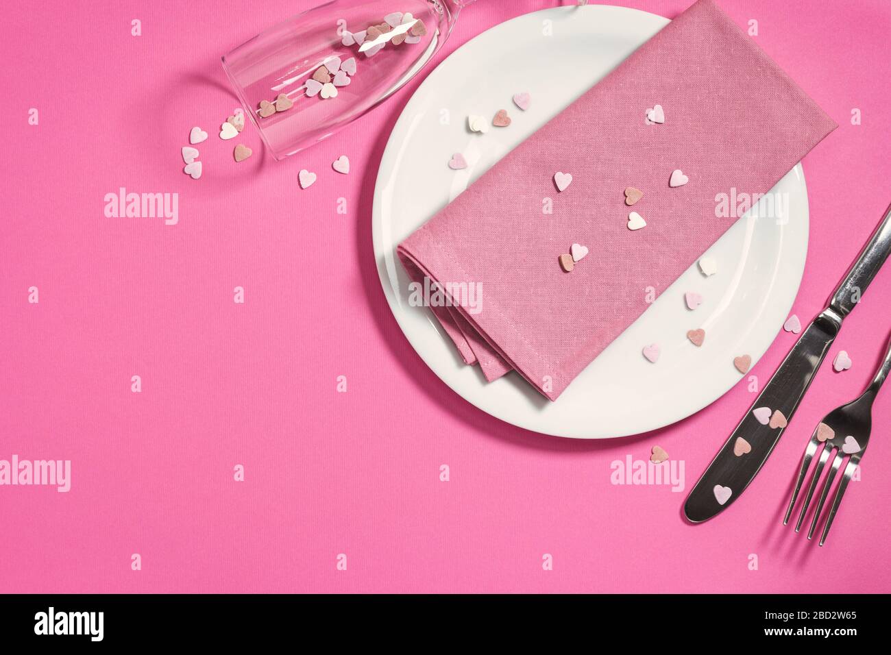 Magnifique table festive avec plaque blanche, serviette et décoration coeurs sur fond rose clair. Vue de dessus avec espace de copie. Banque D'Images