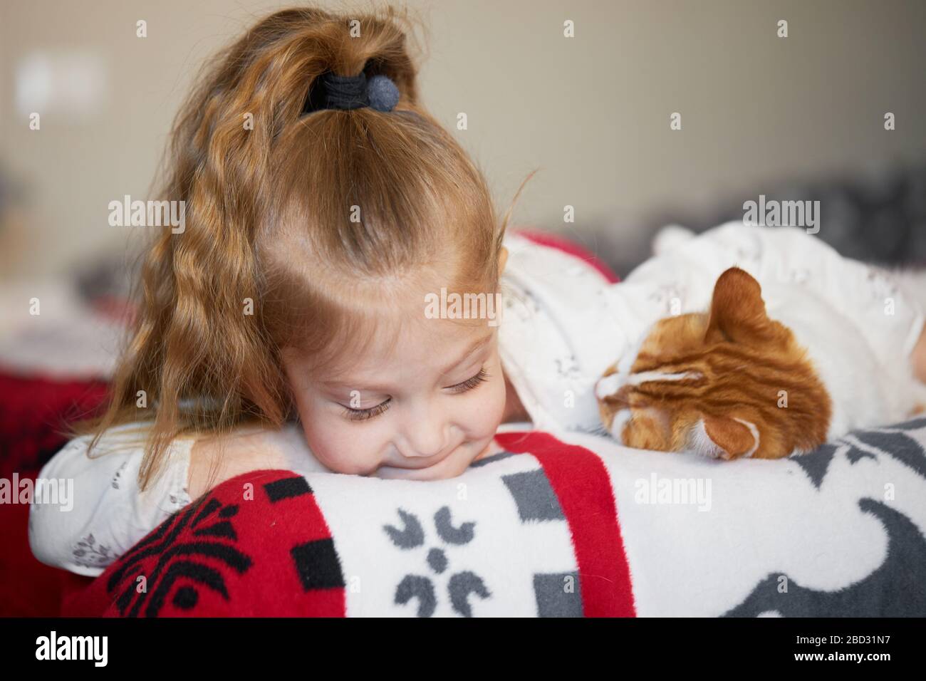 Portrait d'une petite fille d'enfant mignonne qui hople un chat de tête rouge avec tendresse et amour et sourires avec bonheur Banque D'Images