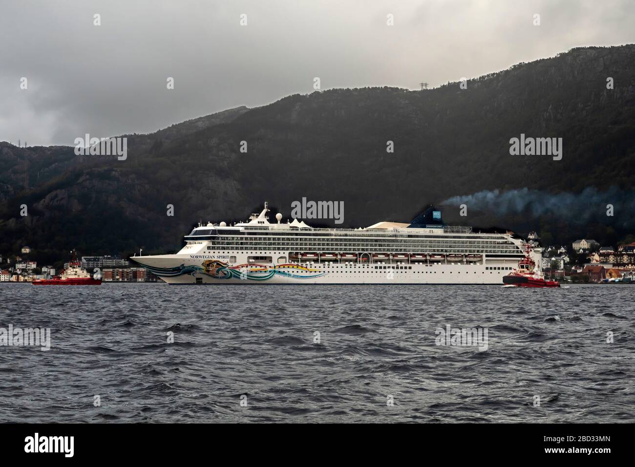 Bateau de croisière Norwegian Spirit au départ du quai de Bontabo, dans le port de Bergen, Norvège. Un jour gris et pluvieux. Deux remorqueurs aident, le travailleur BB et Banque D'Images