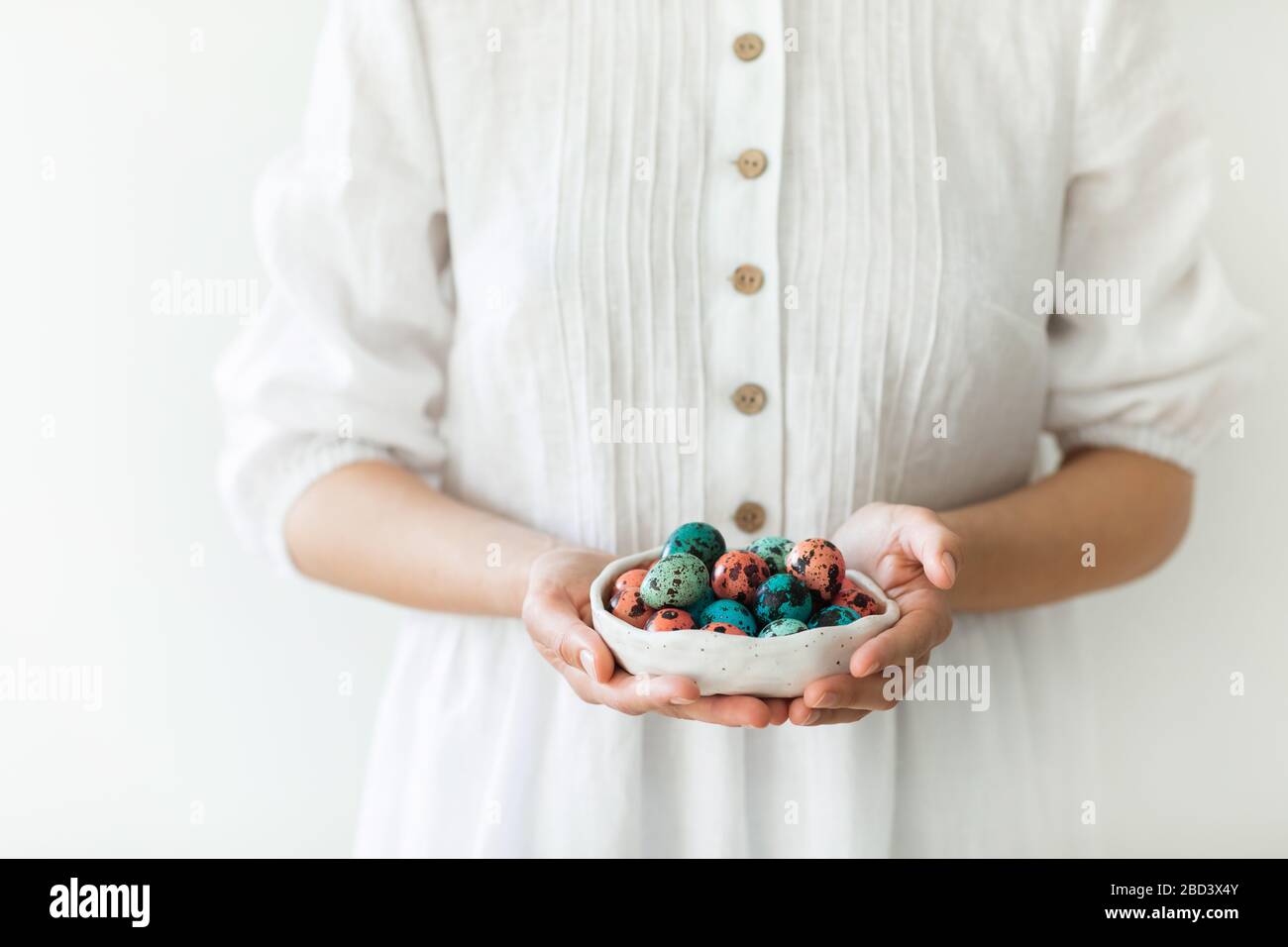 Les mains d'une femme tenant une petite belle plaque en céramique avec des  œufs de caille peints pour Pâques. Robe rustique blanche, couleur rouge et  bleu tendance des œufs Photo Stock -