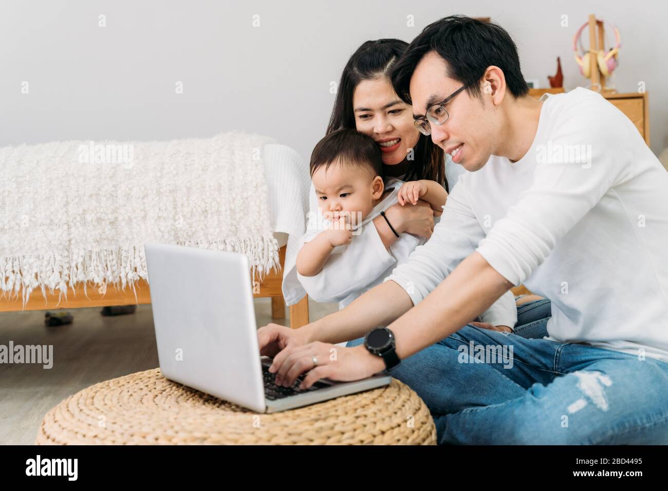 Père asiatique travaillant avec son ordinateur portable avec sa femme et son petit garçon asiatique mignon tout en étant assis au sol dans une chambre confortable à la maison. Banque D'Images