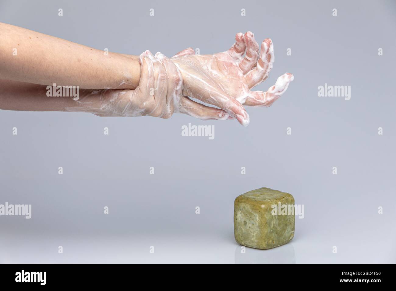 Les mains des blancs se lavant les unes les autres avec le savon de Marseille vert mousse isolé devant un fond gris avec des lumières et des ombres structurantes Banque D'Images