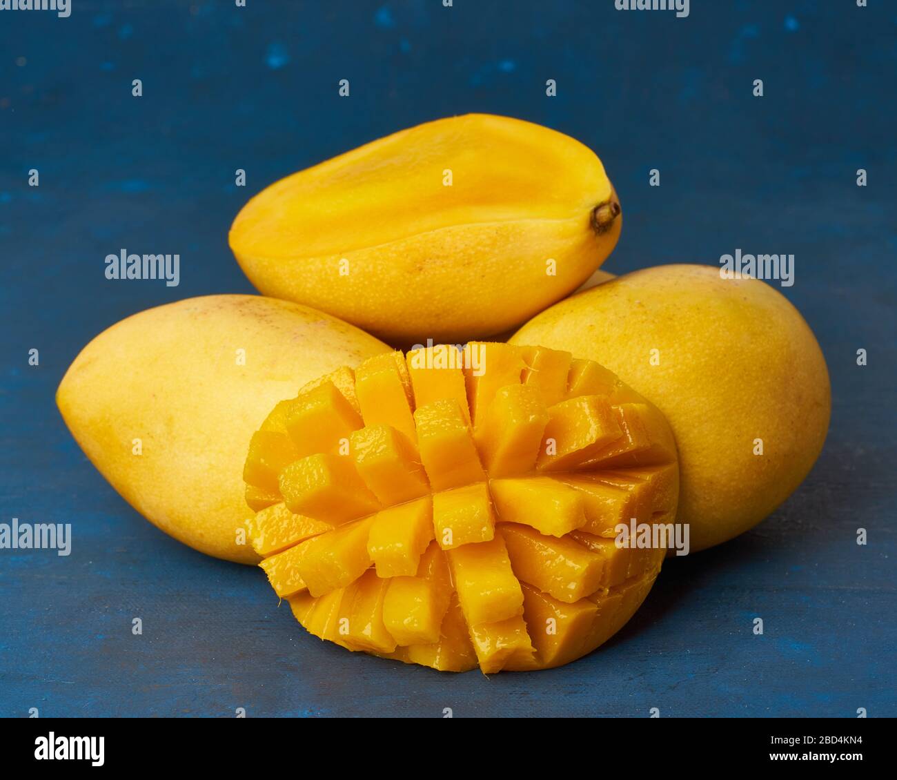 Quatre fruits de mangue entiers sur une table bleu foncé et coupés en tranches. Gros fruits jaunes mûrs juteux Banque D'Images