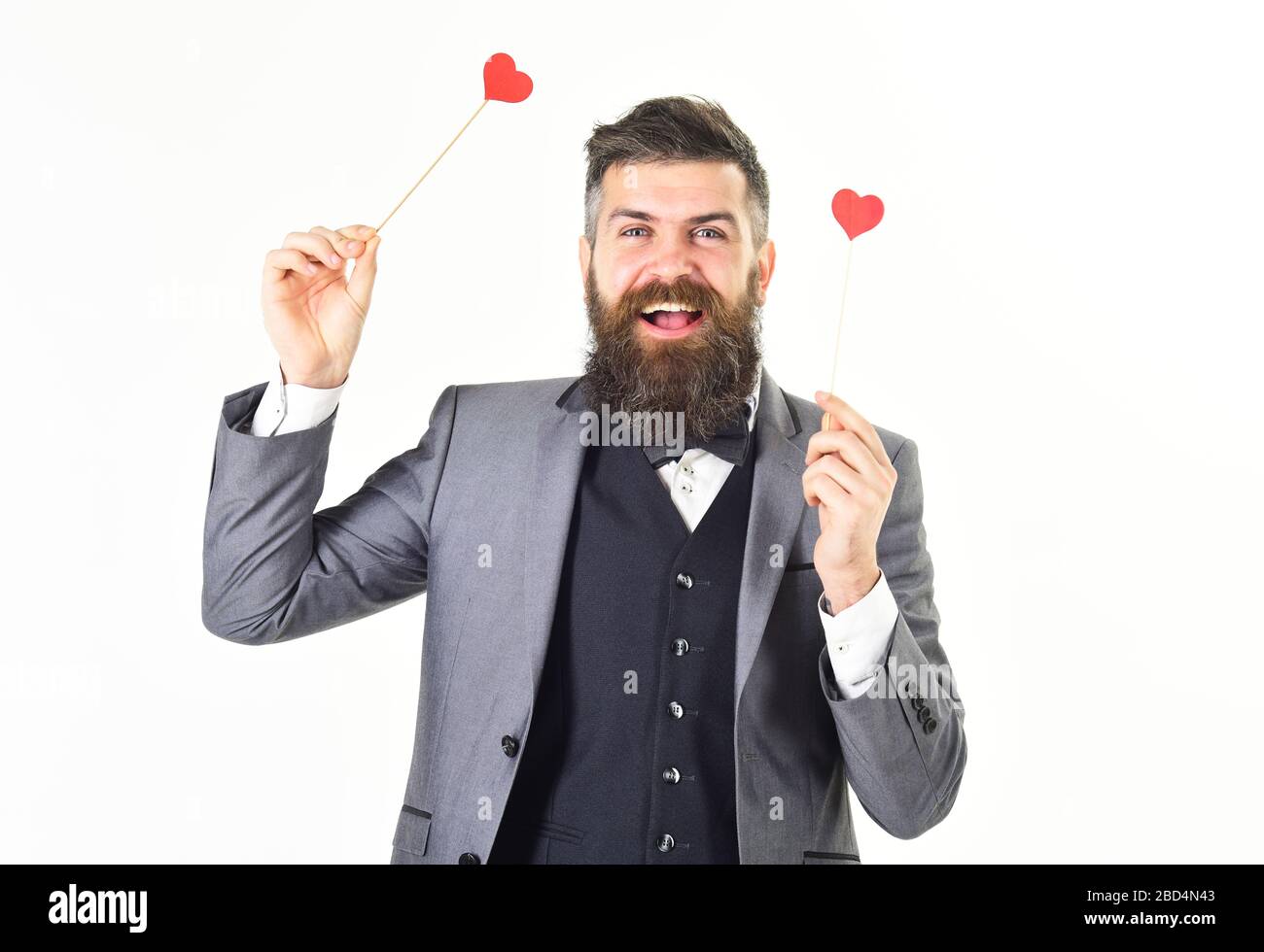 L'Hipster porte un costume élégant et un noeud papillon. Homme mûr avec une  longue barbe et un visage joyeux. Un homme heureux et barbu sourit et tient  des coeurs rouges. Datation, amour,