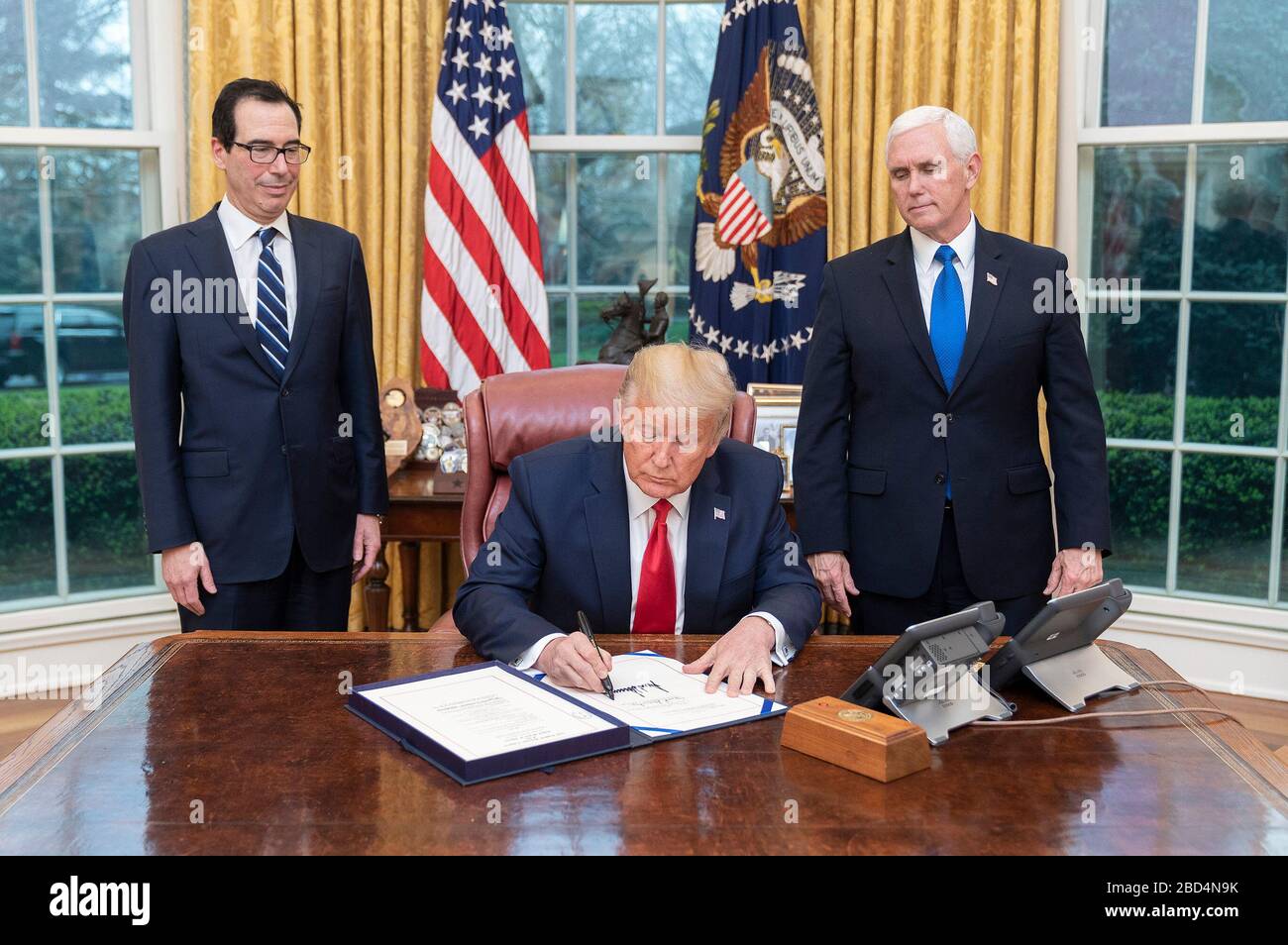 Le résident Donald J. Trump est accompagné du vice-président Mike Pence et du secrétaire au Trésor Steven Mnuchin lorsqu'il signe H.R. 6201, la loi sur la réponse des familles au premier coronavirus, le mercredi 18 mars 2020, au Bureau ovale de la Maison Blanche. Banque D'Images