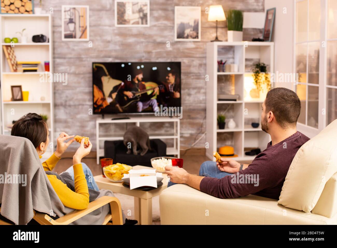 Vue arrière du couple dans le salon à regarder un film sur le téléviseur tout en mangeant de la nourriture à emporter Banque D'Images