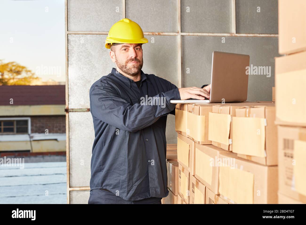 Travailleur avec ordinateur portable dans des boîtes dans l'entrepôt de vente par correspondance Banque D'Images