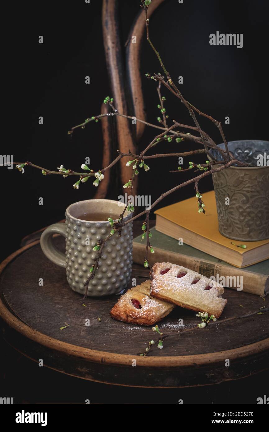 Une tasse de thé et des petits pains faits maison avec des livres et quelques branches d'arbres fleuris sur une chaise ancienne Banque D'Images