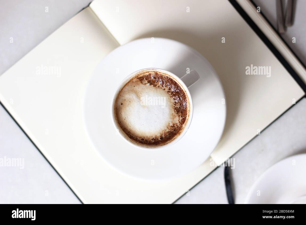 Vue du dessus de la tasse de cappuccino sur un cahier vierge ouvert. Restez à la maison. Banque D'Images