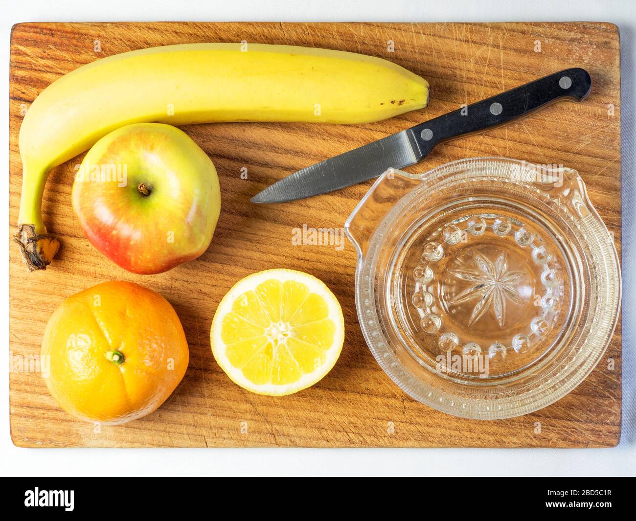 Toujours la vie des ingrédients de salade de fruits orange pomme et banane avec un demi-citron et un couteau de cuisine et un presse-citron sur une planche à découper en bois Banque D'Images