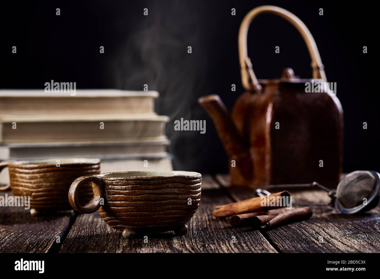 vue rapprochée de la vie en céramique avec tasse de thé ou de café, théière et cannelle. Vieux plan de table en bois, fumée devant les livres et noir flou bac Banque D'Images