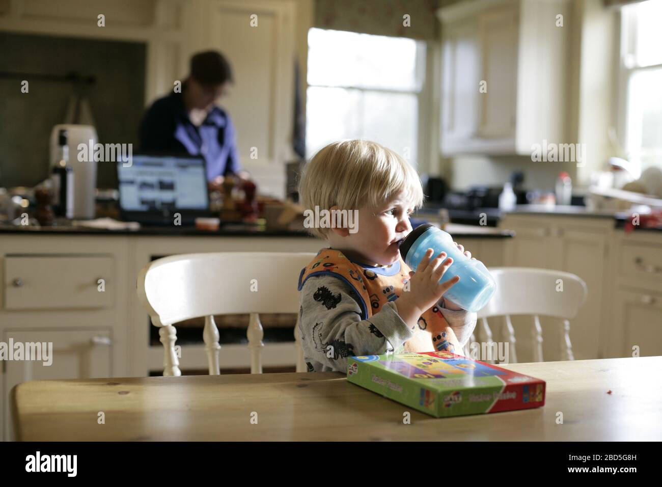 Boisson enfant-enfant à partir de la bouteille de dinks pendant le dîner de cuisine de la mère pendant la période d'auto-isolation - 2020 COVID-19 pandémie de coronavirus Banque D'Images