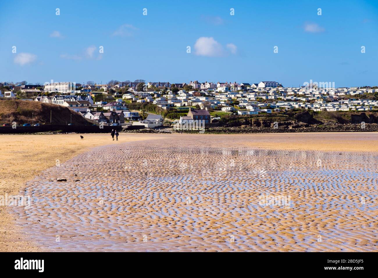 Plage calme avec deux personnes locales marchant pour l'exercice quotidien pendant le verrouillage de Covid-19 en avril 2020. Benllech Isle of Anglesey Wales Royaume-Uni Grande-Bretagne Banque D'Images