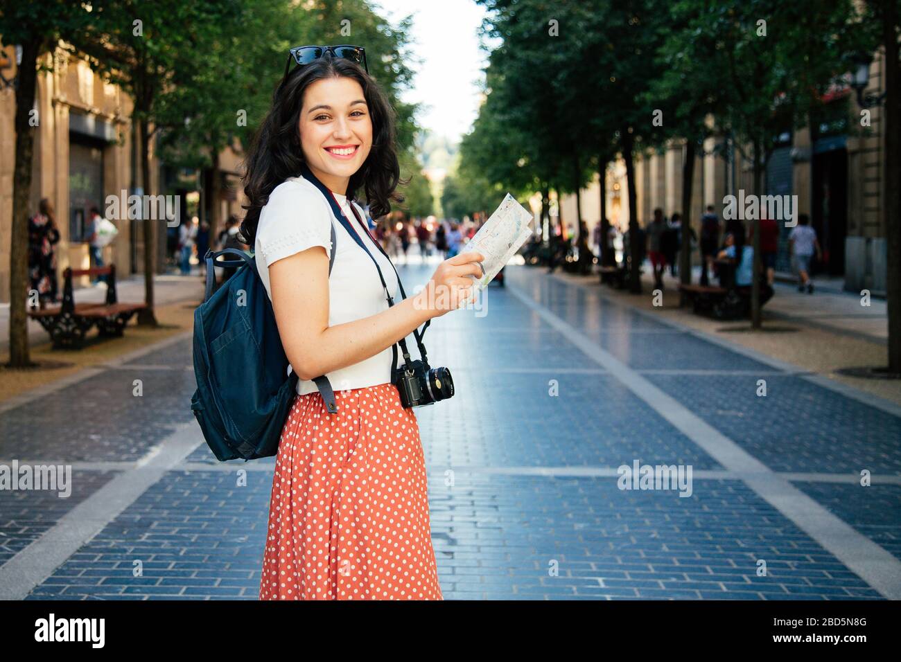 Une femme de tourisme heureuse avec sac à dos, appareil photo et carte visitant la ville souriant Banque D'Images