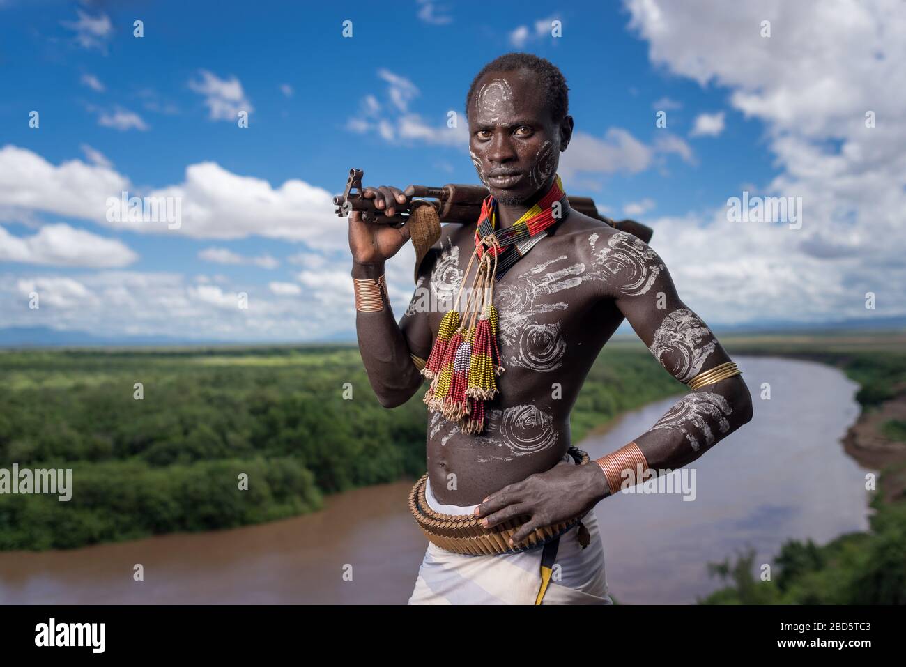 Affichant sa carabine et sa peinture corporelle au-dessus de la rivière Omo, une tribu Karo ou un membre d'un groupe ethnique, Tumi, Ethiopie. Banque D'Images