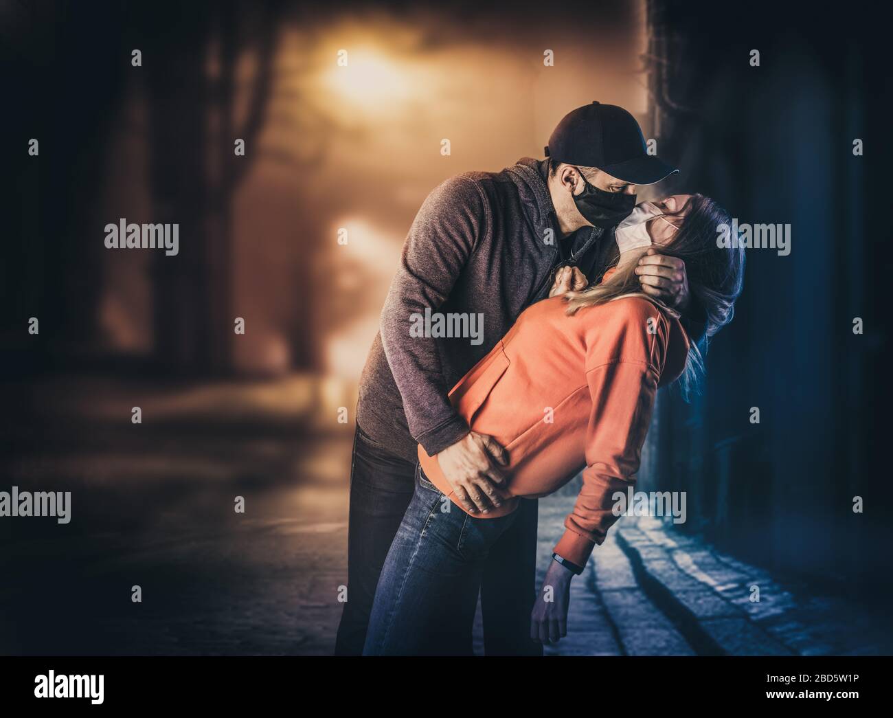 Un jeune homme adulte embrasse une femme dans des masques médicaux protecteurs dans une rue de ville la nuit. Concept de victoire et d'amour de coronavirus Banque D'Images